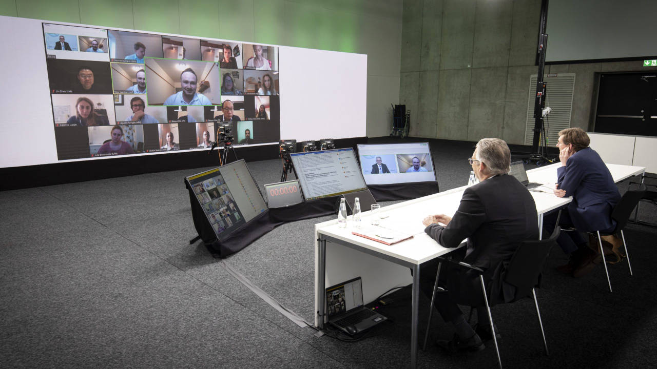 Moderatoren der GFFA blicken auf einen Bildschirm, der weitere Teilnehmer der Videokonferenz zeigt.