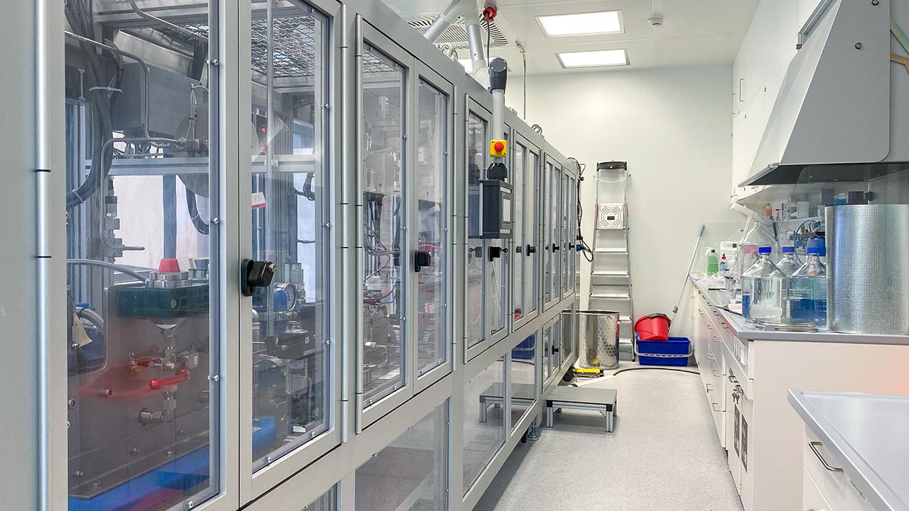 Blick in ein Labor mit Werkbänken rechts und links Apparturen in Metall-Glas-Schränken