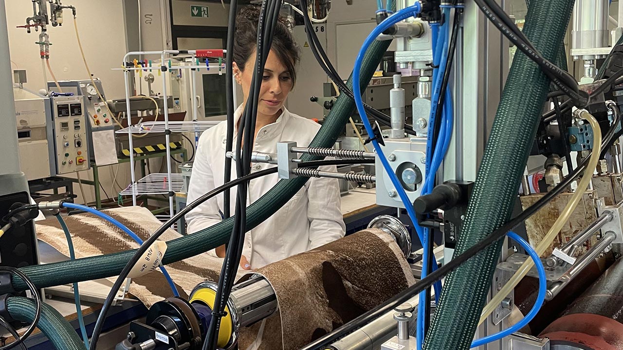 Eine Frau steht hinter einer Maschine, die ein Stück Stoff verarbeitet