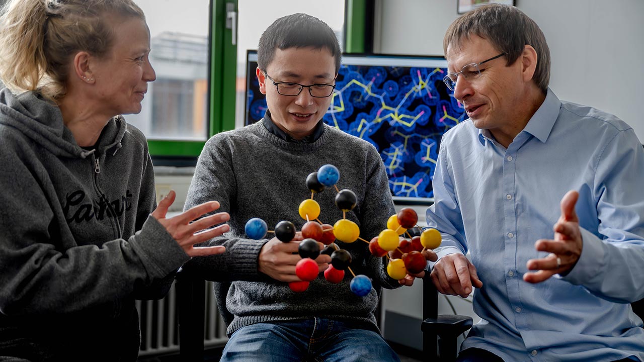 Eine Frau (links) und zwei Männer diskutieren über ein Molekülmodell, das der Mann in der Mitte in der Hand hält.