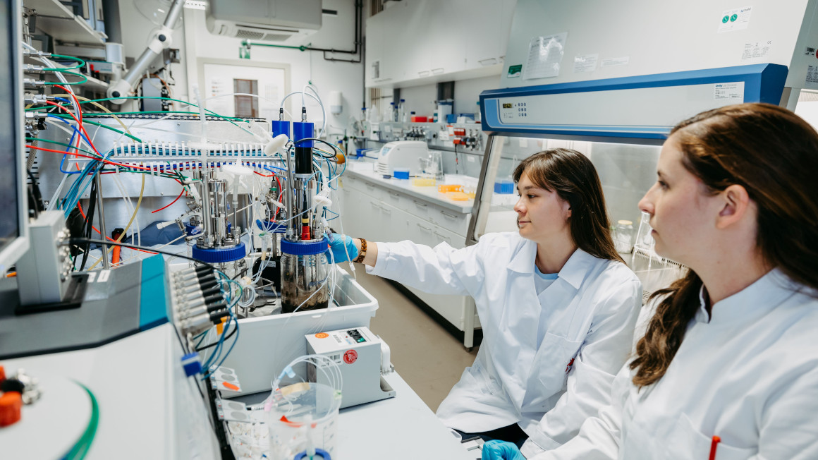 Stefanie Duvigneau (rechts) und Anna-Sophie Neumann (links) arbeiten gemeinsam im Labor an der Biopolymerproduktionsanlage.