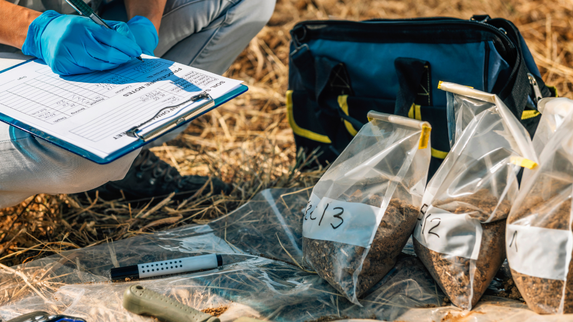 Eine Forscherin entnimmt und beschriftet Bodenproben auf einem Feld.